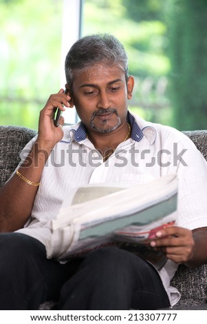 indian mature male on phone conversation while reading newspaper with lifestyle background