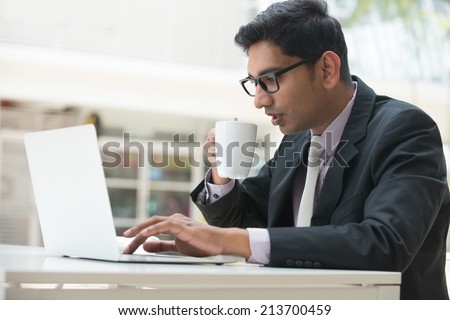 young indian business male on laptop and coffee at a cafe