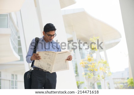 Indian man checking on new office to let, holding newspaper and calling on phone.