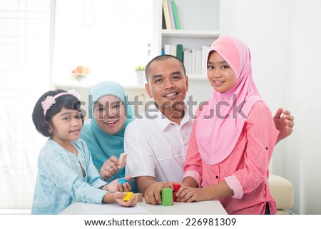 Malay family at home. Muslim girl building a wooden toy house. Southeast Asian parents and child living lifestyle.