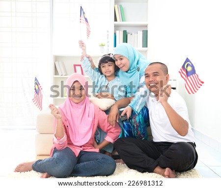 malaysian family celebrating while watching television over a tournament , some are carrying country flags