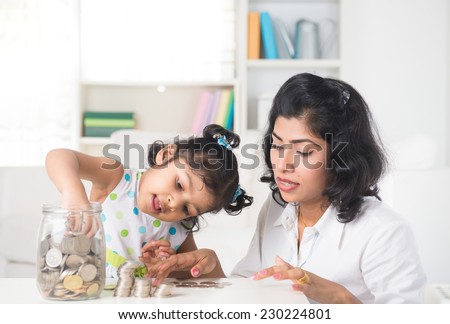 indian Mother and daughter putting coins into bottle, saving plan