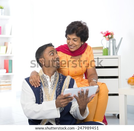 Mature 50s Indian woman and son using digital computer tablet at home