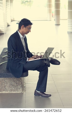Asian Indian businessman using laptop computer while waiting train at railway station.