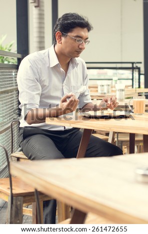 Asian Indian business man reading newspaper while drinking a cup hot milk tea during lunch hour at cafeteria.