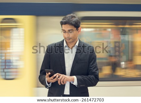 Asian Indian businessman texting using smartphone while waiting train at railway station