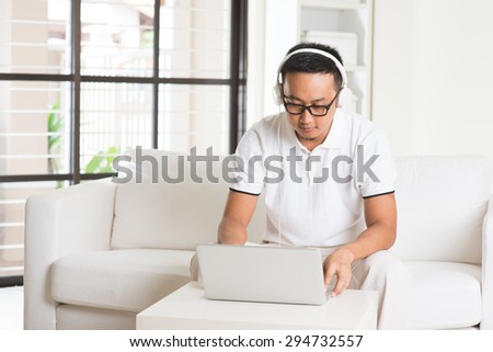 Handsome Asian man using tablet computer. Smiling Southeast Asian college student relaxing and listening to music at home. Asian model.