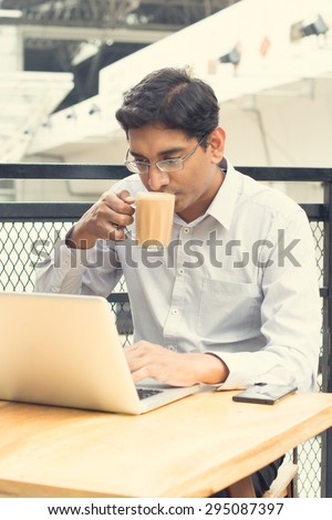 Asian Indian businessman using laptop computer while drinking a cup hot milk tea.