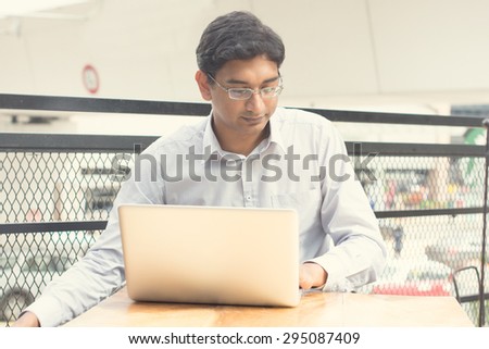 Asian Indian businessman sitting on chair and using laptop while waiting his flight at airport.