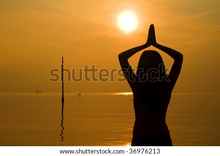 young asian women poses yoga/pray on beach with silhouette of a sunset