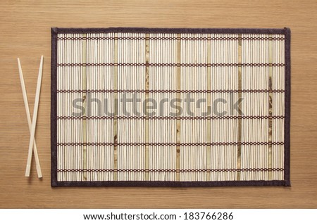 Bamboo mat with chopsticks on table as background for food composition
