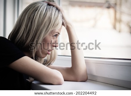 Stressed young woman looking through window outside