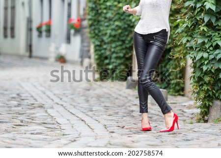 Woman wearing black leather pants and red high heel shoes in old town