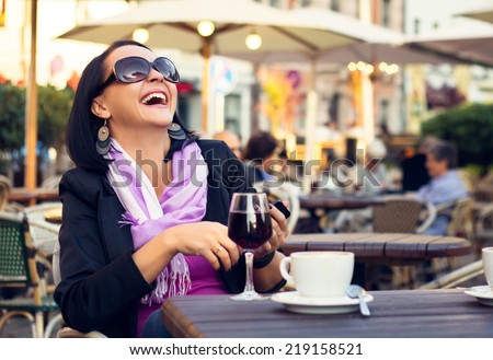 Happy woman enjoying evening with coffee and wine in outdoor cafe