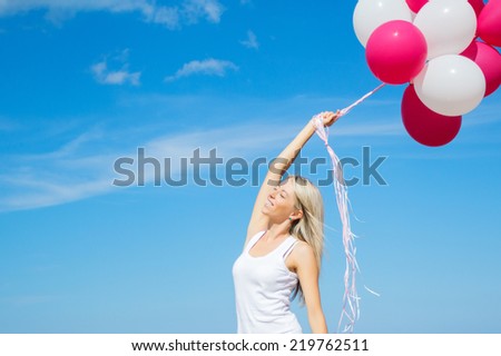 Happy young woman holding balloons in clear blue sky