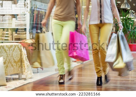Two women walking along shop windows with shopping bags in hands