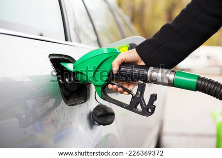 Close-up photo of hand holding fuel pump and refilling car at petrol station