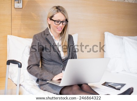 Business woman in suit sitting in bed and working with computer in hotel room