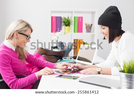 Two relaxed creative young women using tablet computer in the office