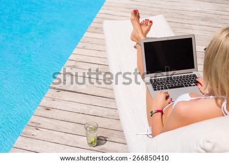 Woman working with laptop computer by the swimming pool