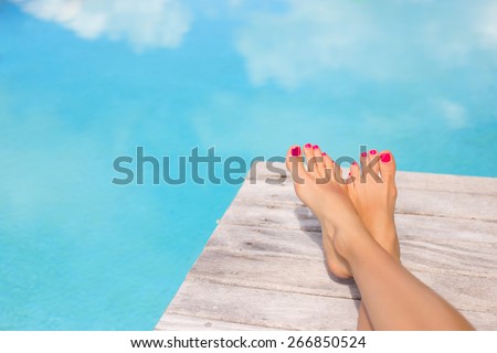 Bare woman feet on wooden deck by the swimming pool
