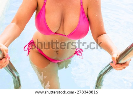 Curvy woman in pink bikini getting out of swimming pool