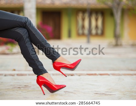Woman in black leather pants and red high heel shoes sitting on bench