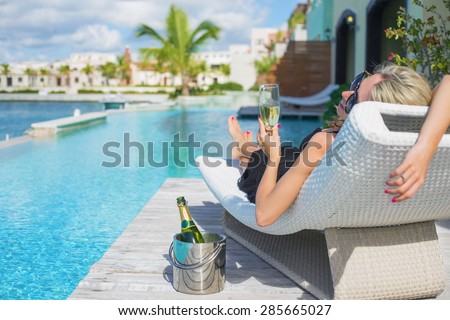 Lady relaxing in deck chair by the pool and drinking champagne
