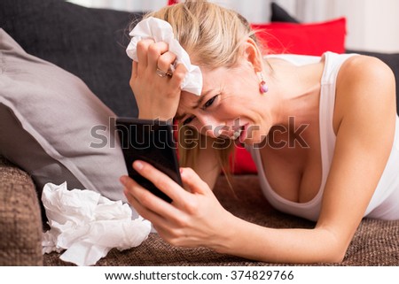 Woman crying while lying on couch with cellphone in her hand