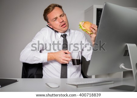 Busy man at the office having coffee and burger