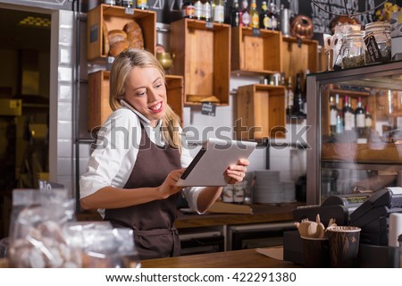 Female barista talking on the phone and using tablet while standing behind the counter