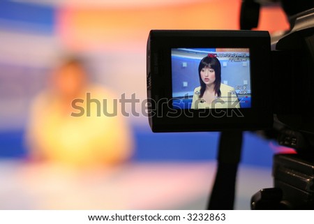 Young woman TV reporter presenting the news, view in video camera display