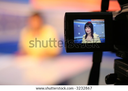 Young woman TV reporter, smiling and presenting the news, view in video camera display