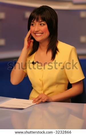 Young woman TV reporter smiling and listening in earphone while preparing for the news presenting