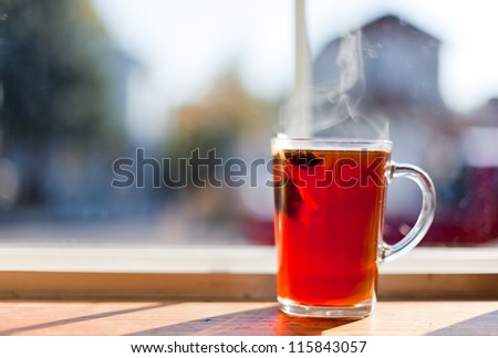 A clear glass cup of hot tea with a floating tea bag and a anise star with steam rising. blurred domestic background.