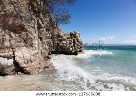 A natural rock formation with a small cave carved out from the force of waves hitting it through the years. Blue sky background.