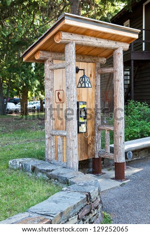 A public telephone booth made from logs and boards with a sloped roof and hanging lamp in Glacier National Park, Montana.