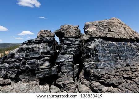 A large formation of black obsidian lava flow cracked by weather and erosion in Newberry National Volcanic Monument, Oregon.