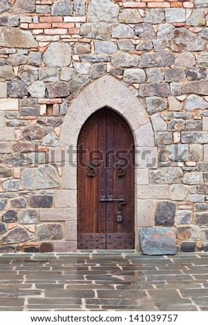 A medieval wooden door with metal accents and a metal lock framed by carved rocks in a rock and brick wall of a castle interior.