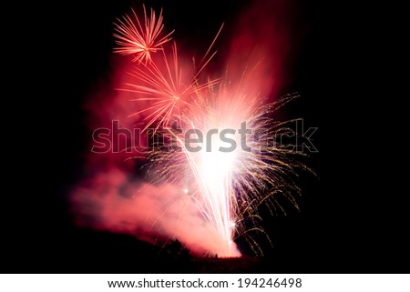 A man stands under a large display of vibrant fireworks as they are set off.