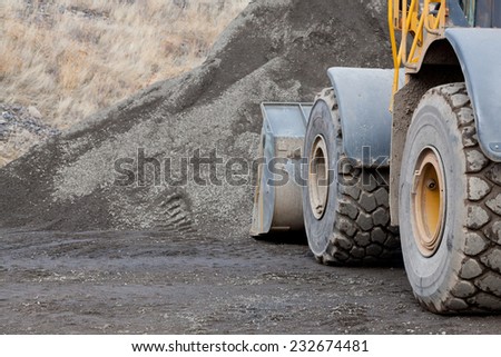 Large wheels and the bucket of a construction loader up against a pile of gravel at a job site.