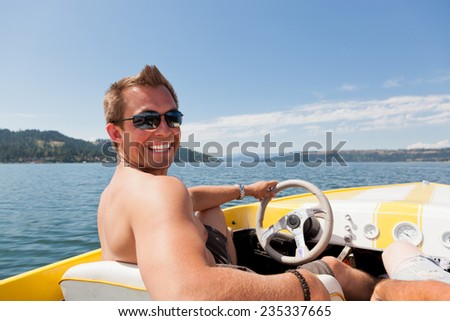 A smiling handsome young man behind the wheel of a yellow speedboat on Lake Coeur d\'Alene, ID.