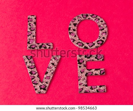 Glitter covered letters in a leopard pattern spell out love in a block pattern on a bright pink paper background.