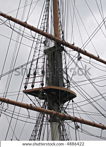 Mast and rigging on an old wooden ship against a grey, foreboding sky