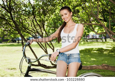 A beautiful young girl in a white T-shirt and blue jeans is sitting a bicycle - Outdoors