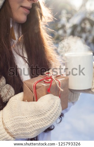 woman drinking tea and holding a gift in hand on a background of a winter landscape, outdoors