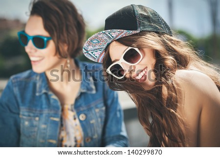 Two beautiful happy girls in sunglasses on the urban background. Young active people. Outdoors