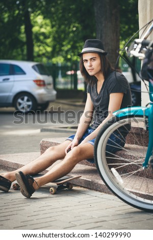 Man with skateboard sitting on stairs. Young active people. Outdoors