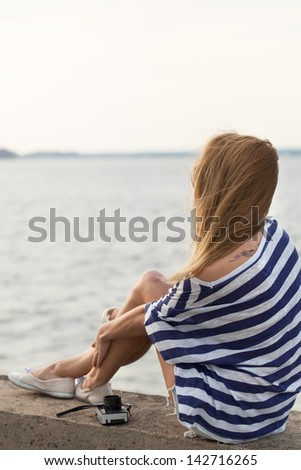 Young woman with old camera sitting on pier near sea. Outdoor, lifestyle