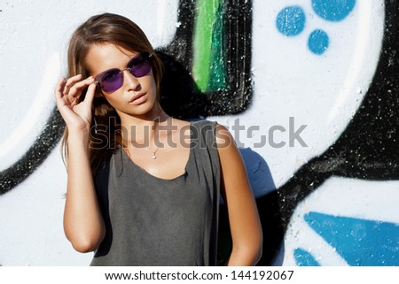 Beautiful woman with sunglasses near a wall with graffiti. Outdoors